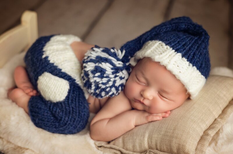 A peaceful newborn boy sleeping soundly in a cozy blue knitted outfit.