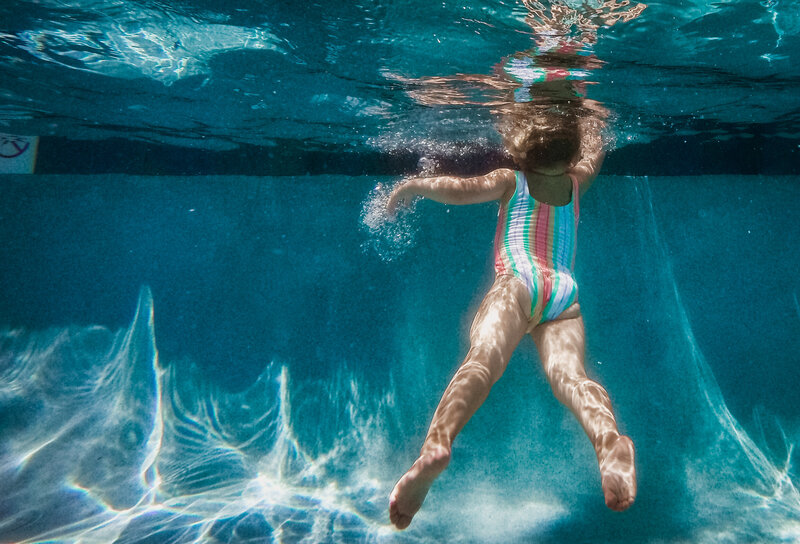 Little girl swimming underwater reaching at the surface