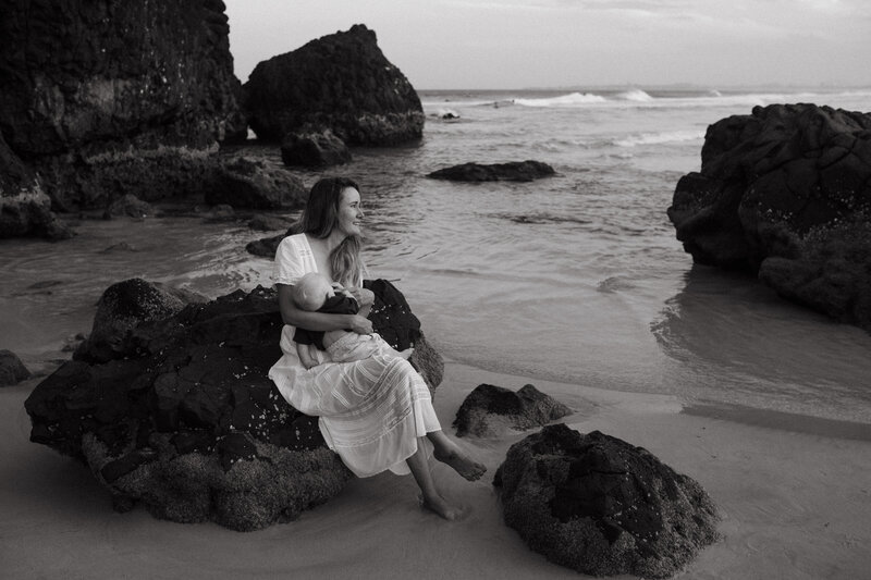 A mother feeds her baby at Dreamtime Beach , she out at the waves 