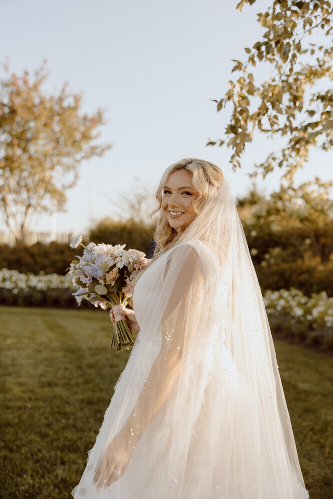 Bride poses in floral wedding dress in a a field while its raining