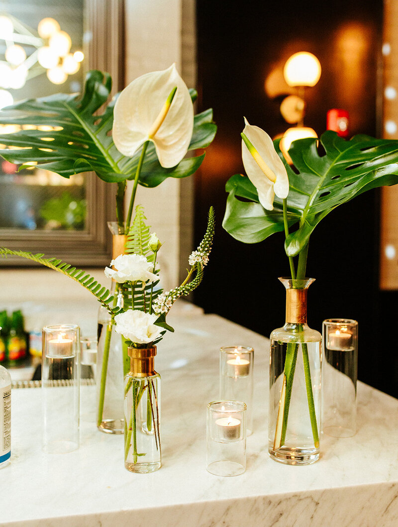 white anthurium with philodendron leaves in clear glass vases