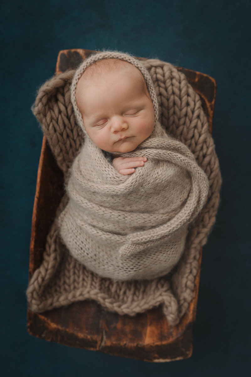 Baby boy in small bed wrapped and holding a knitted bunny