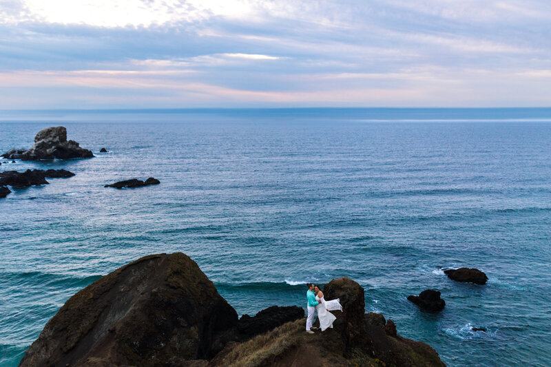 Couple standing on a rocky outcrop with panoramic ocean views, photographed by an Oregon Coast Elopement and Wedding Photographer.