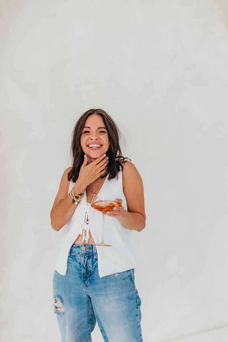 Laughing web designer holding a glass of champagne spilling over-celebrating bold ideas and Latina vibes.
