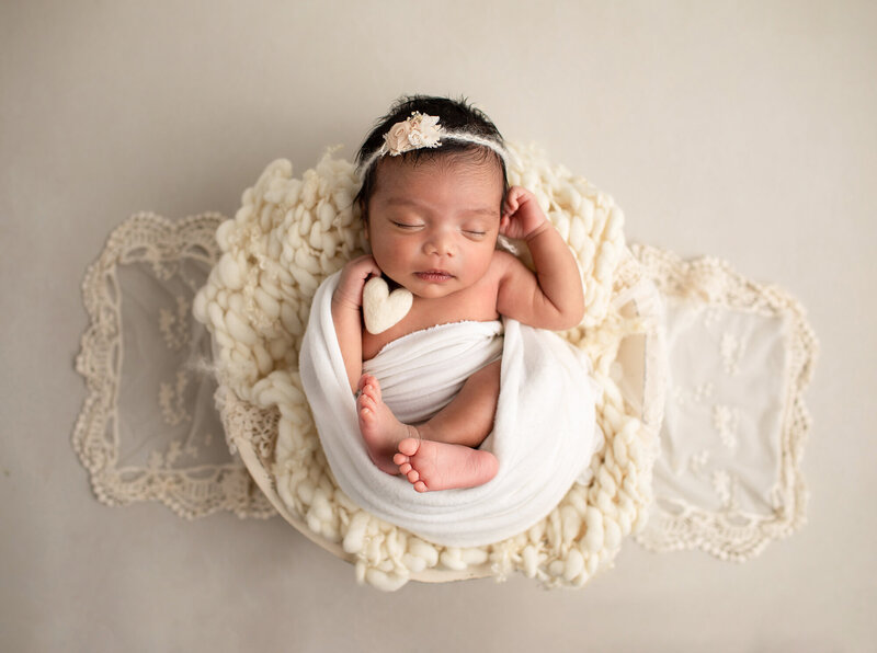 Baby girl swaddled with feet out holding a cream colored heart  for newborn photography columbia md