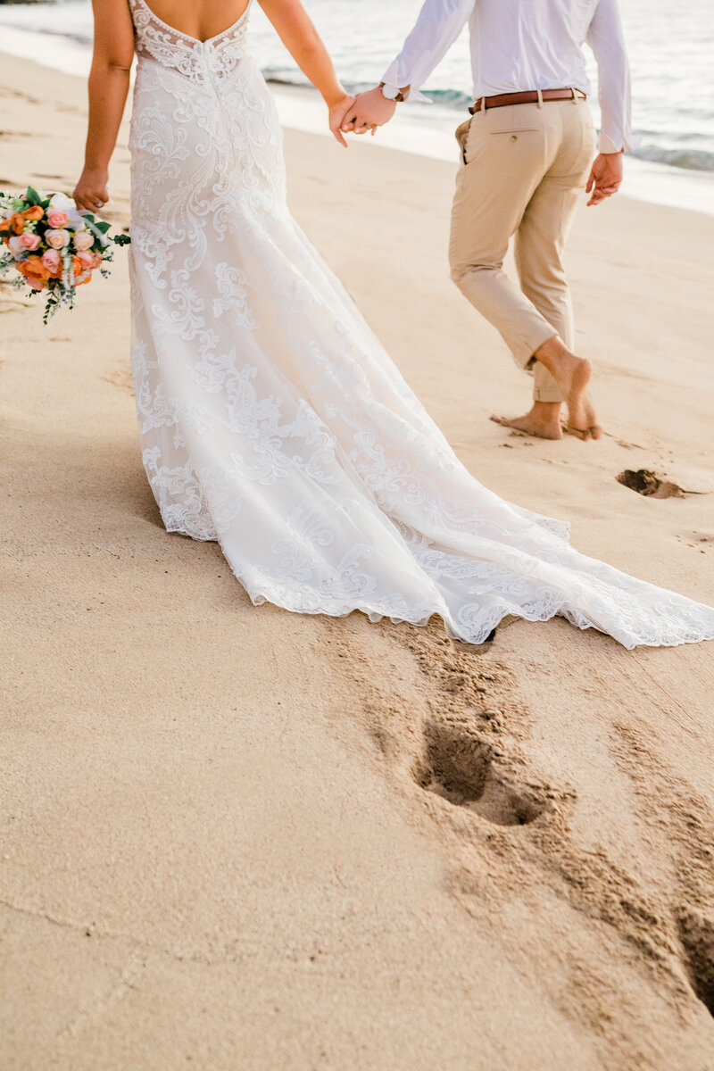 bride and groom holding hands walking in sand