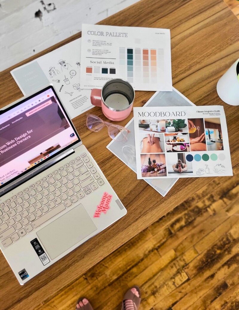 Laptop on wooden desk with mood board, color palette, and coffee cup for SEO and branding strategy work