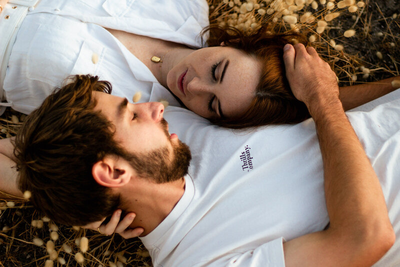 Couple laying in patch of dandelions shoulder to opposite shoulder & touching each others heads