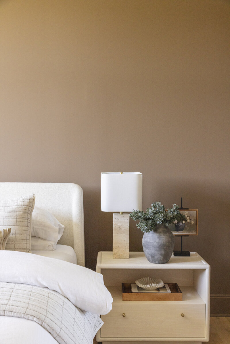 Modern, neutral-toned bedroom interior with a styled nightstand and cozy bedding, representing San Diego home buying inspiration — Mary Pernicano Real Estate.