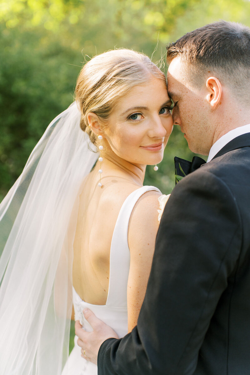 An intimate outdoor wedding ceremony under hanging lanterns with dappled sunlight filtering through the trees.