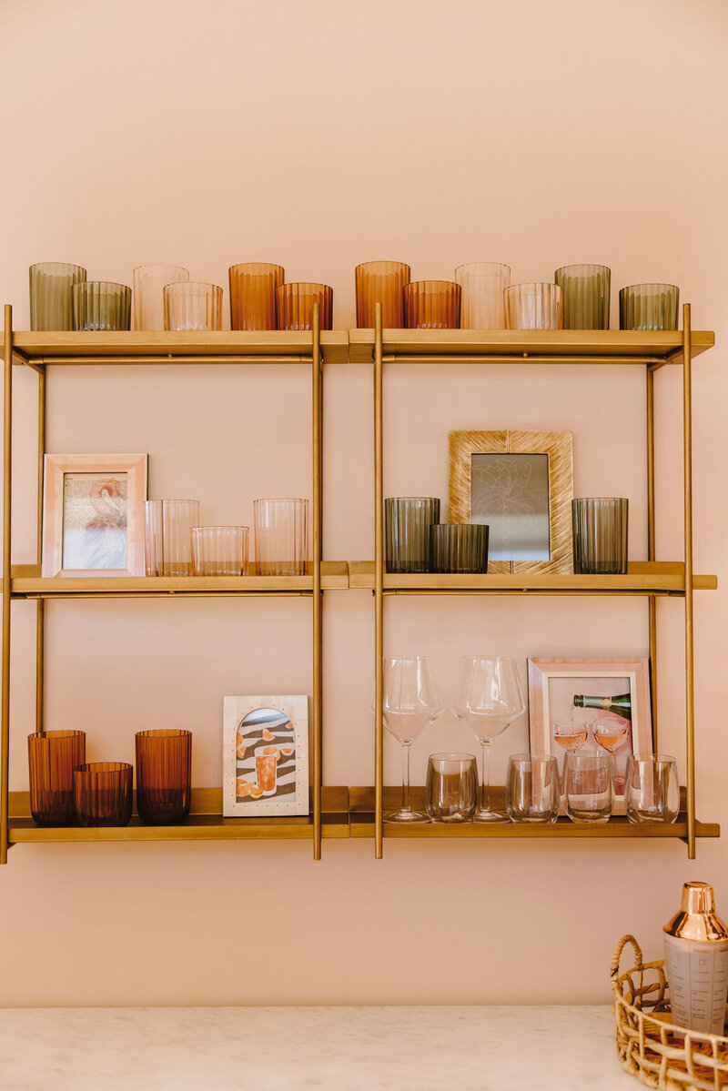 gold metal shelves  with glasses against pink wall