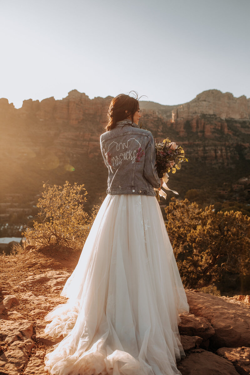 bride in denim jacket in sedona with purple and green bouquet and full trail wedding dress
