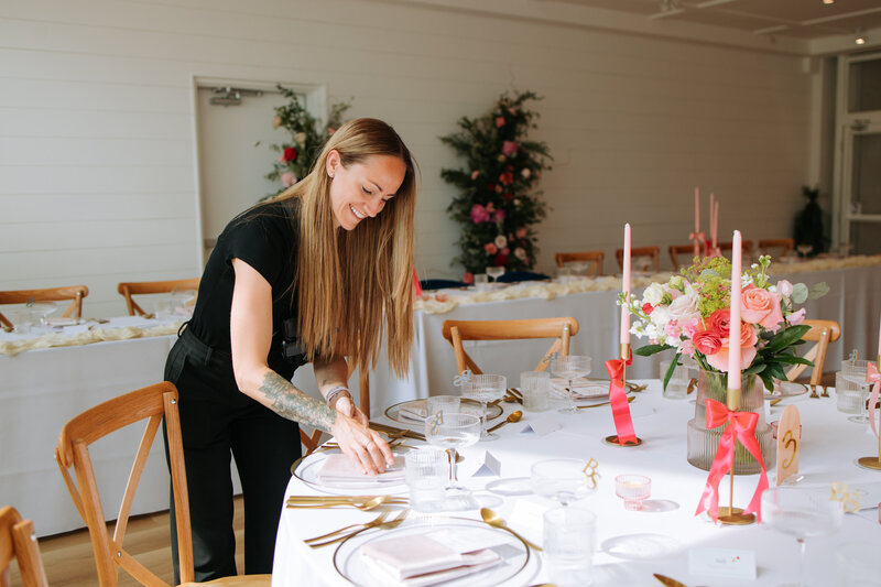 Wedding planner setting an elegant reception table with florals, candles, and gold flatware — showcasing professional wedding planning services in Canmore.