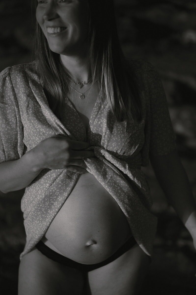 Gravid kvinna visar sin mage med att hålla upp klänningen och ler.