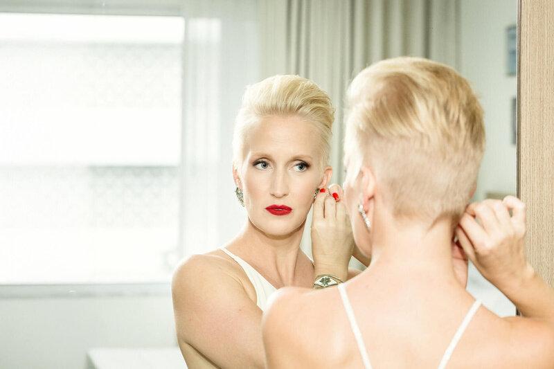 Bride putting on her earrings in front of a mirror during final preparation for First Look wedding photos as part of her wedding day photo timeline.