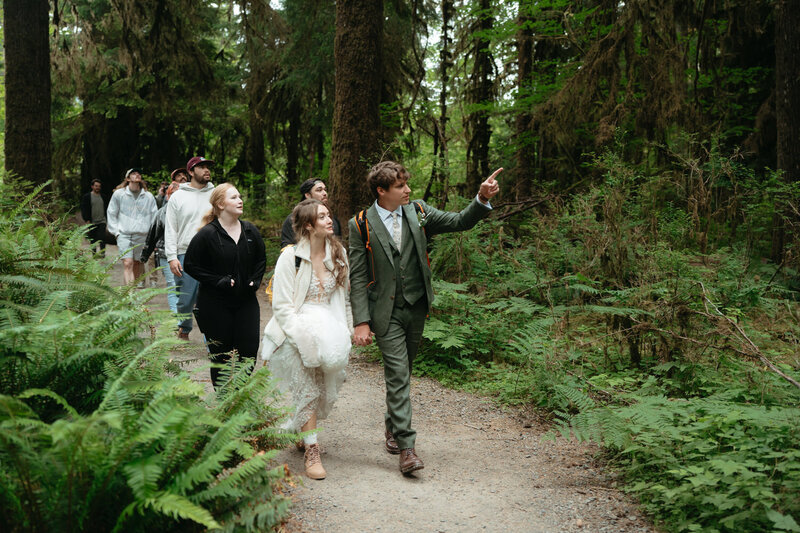 Elopement Ideas with Family | Eloping couple leads their family on a hike through the forest, groom is pointing out a tree 