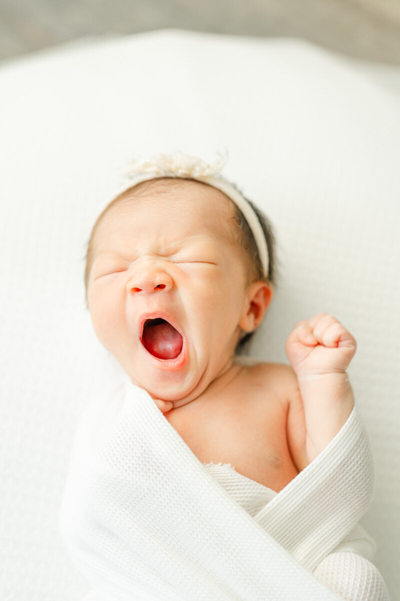 a newborn girl yawns while sleeping on a white surface during her newborn session with an Austin photographer.