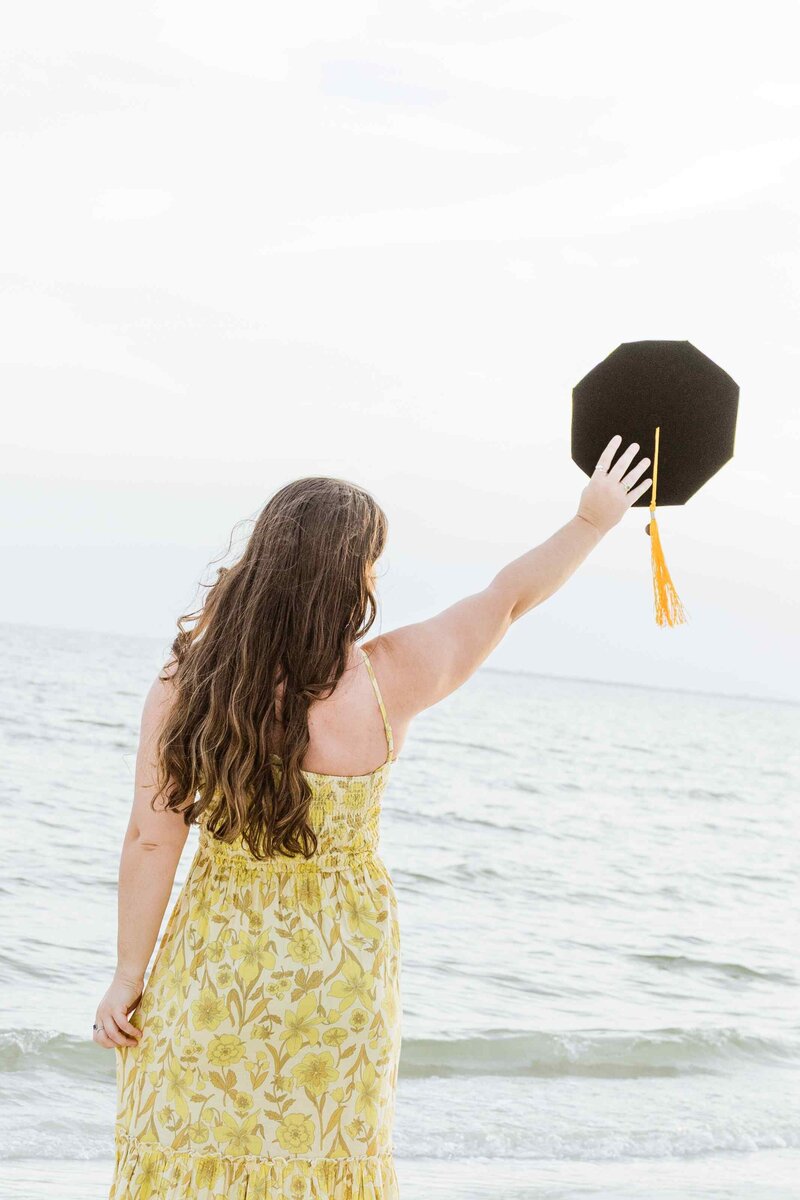 Graduate lifts cap up with ocean in the background