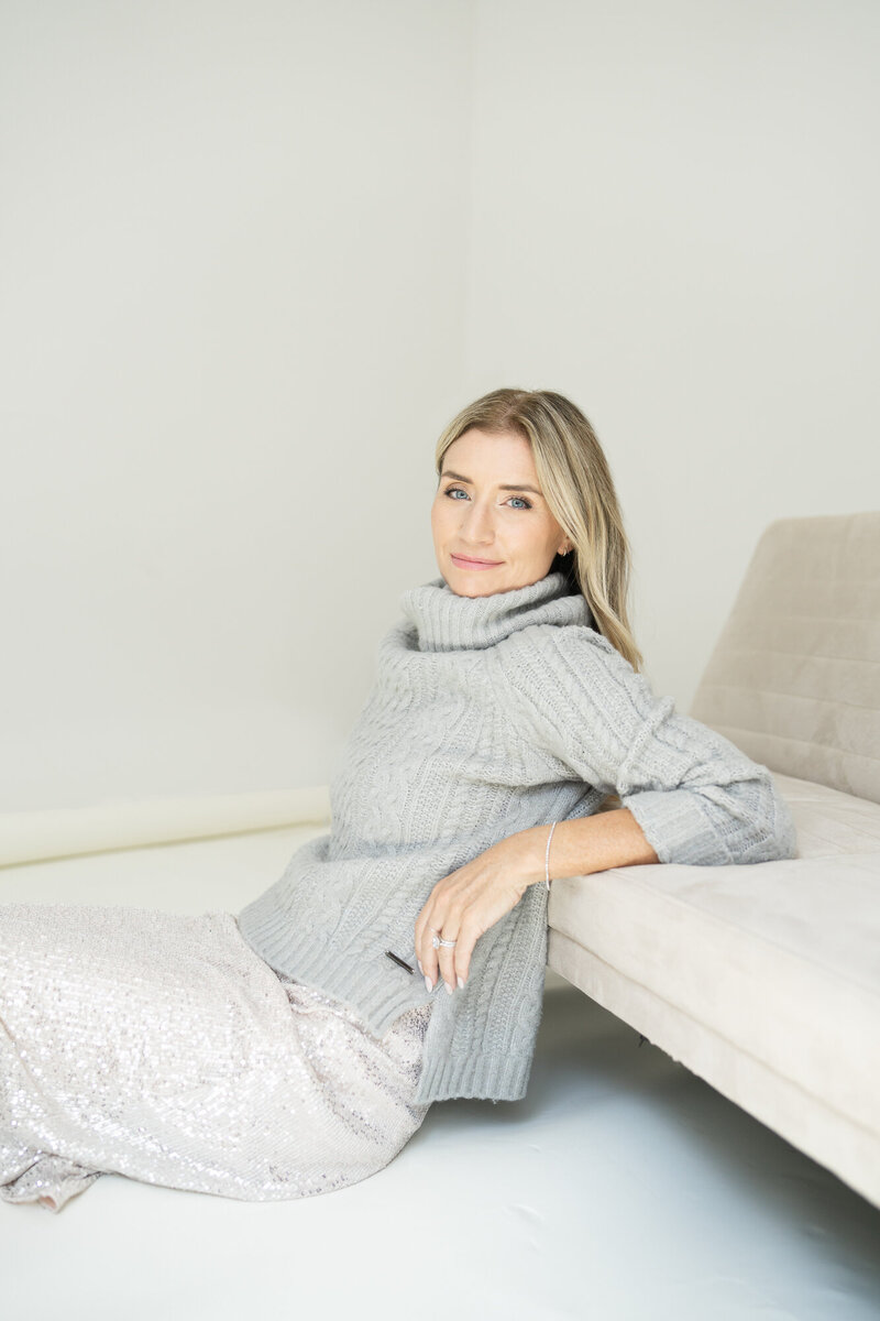 Corporate coach Wendy Tamis Robbins wearing a white sweater sitting on a grey armchair