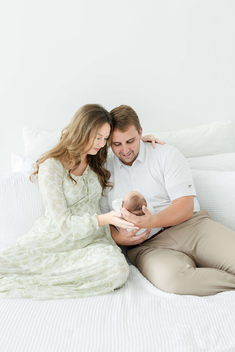 Mom and Dad embracing while holding and smiling at newborn baby during newborn photography session in Dothan Alabama photography studio
