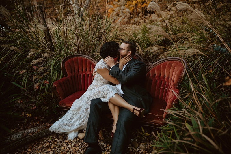 bride and groom kiss on a vintage red couch 