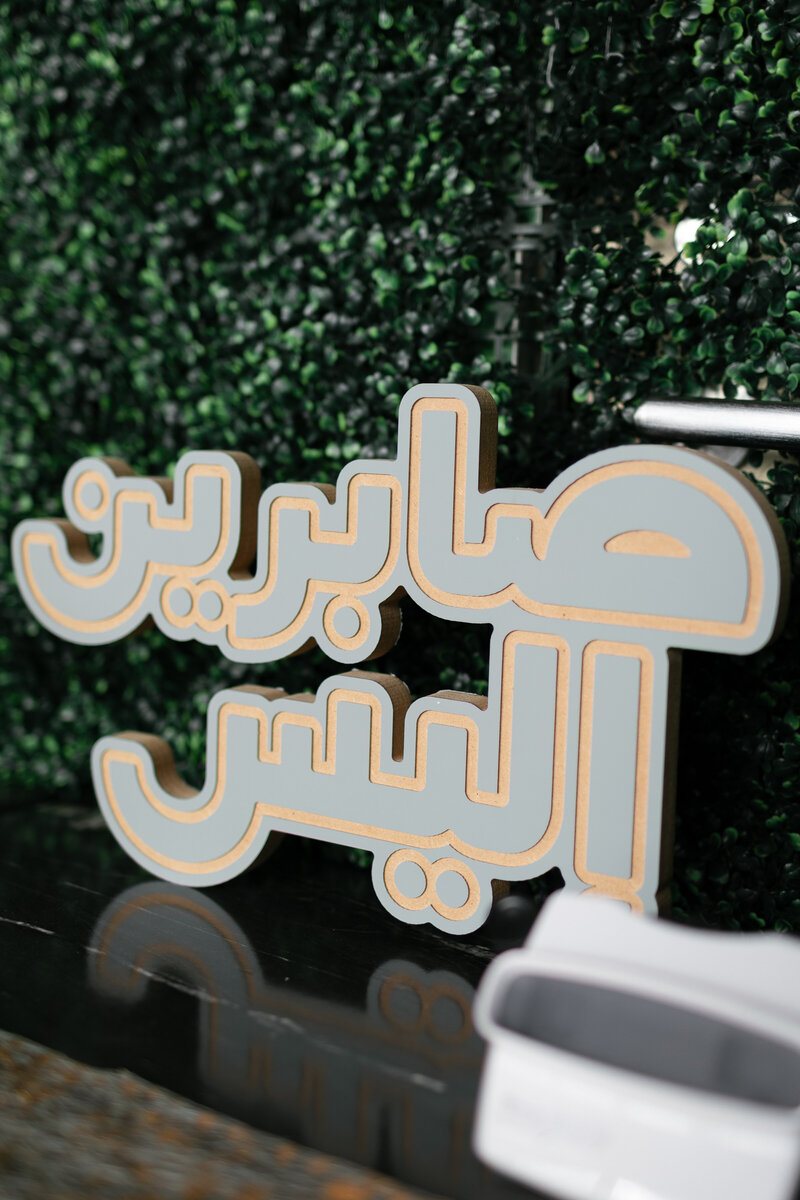 wooden painted light blue with pale yellow outlining the letters of an arabic sign that says Sabreen &  Ellysse