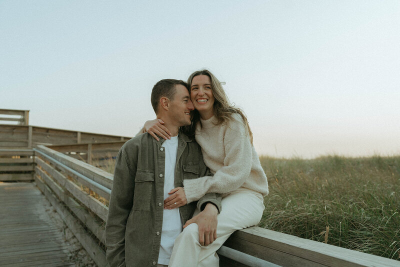 couple with arms around each other during beach engagement photos, captured by Elsie Goodman, an NYC engagement and couples photographer