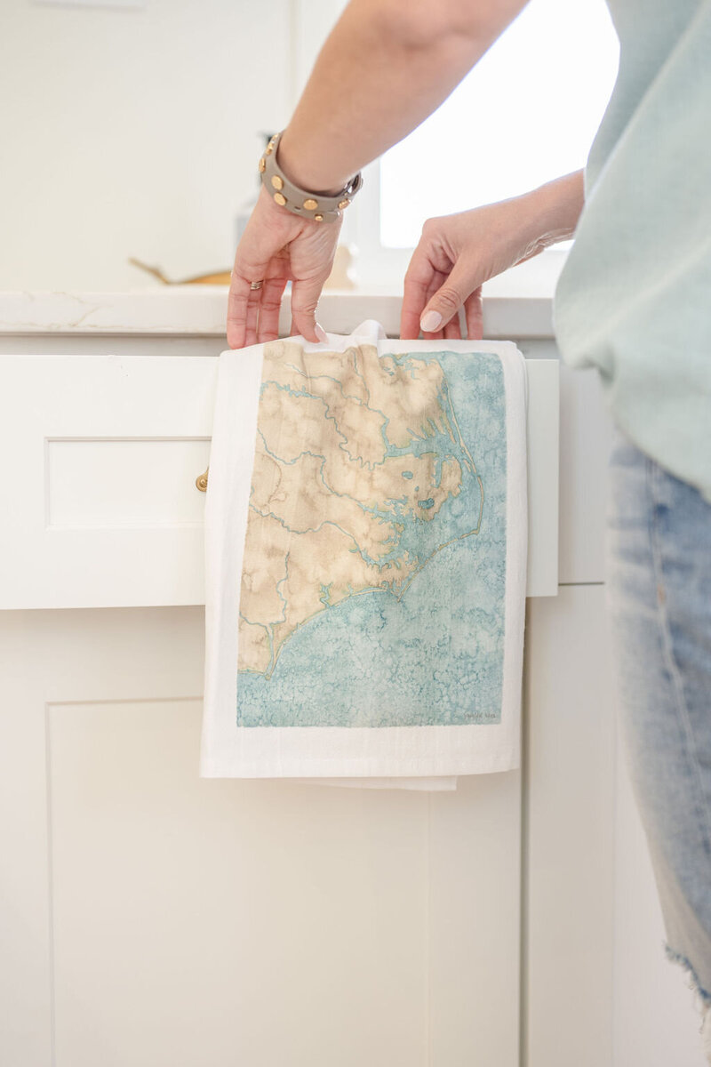 a watercolor painting of coastal map printed on a tea towel hanging over a white drawer in a kitchen