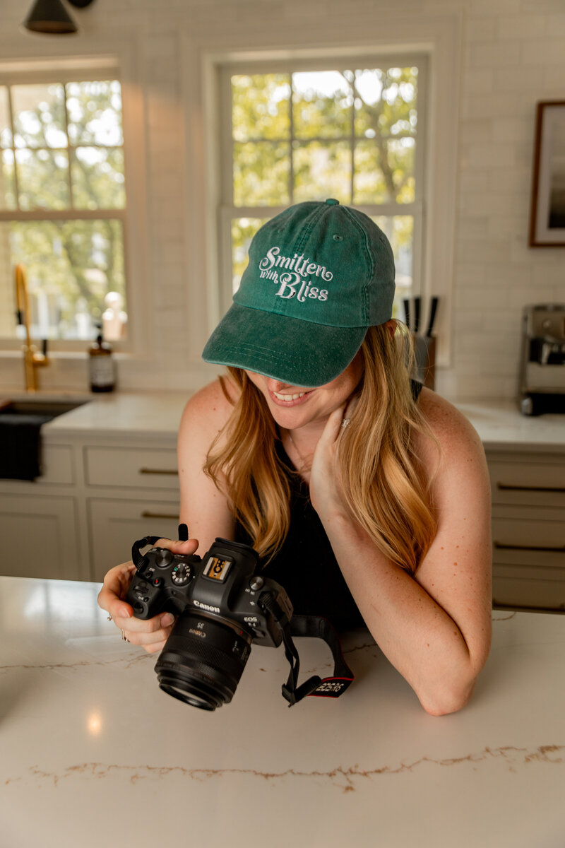 Image of Brook wearing a Smitten with Bliss hat, looking at the back of her camera while smiling.