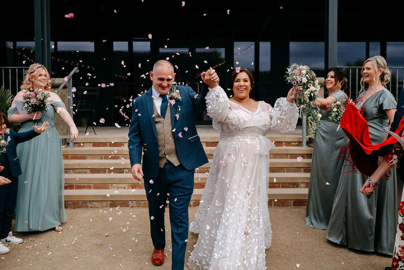 couple throw their hands in the air whilst being covered in confetti at grangfields