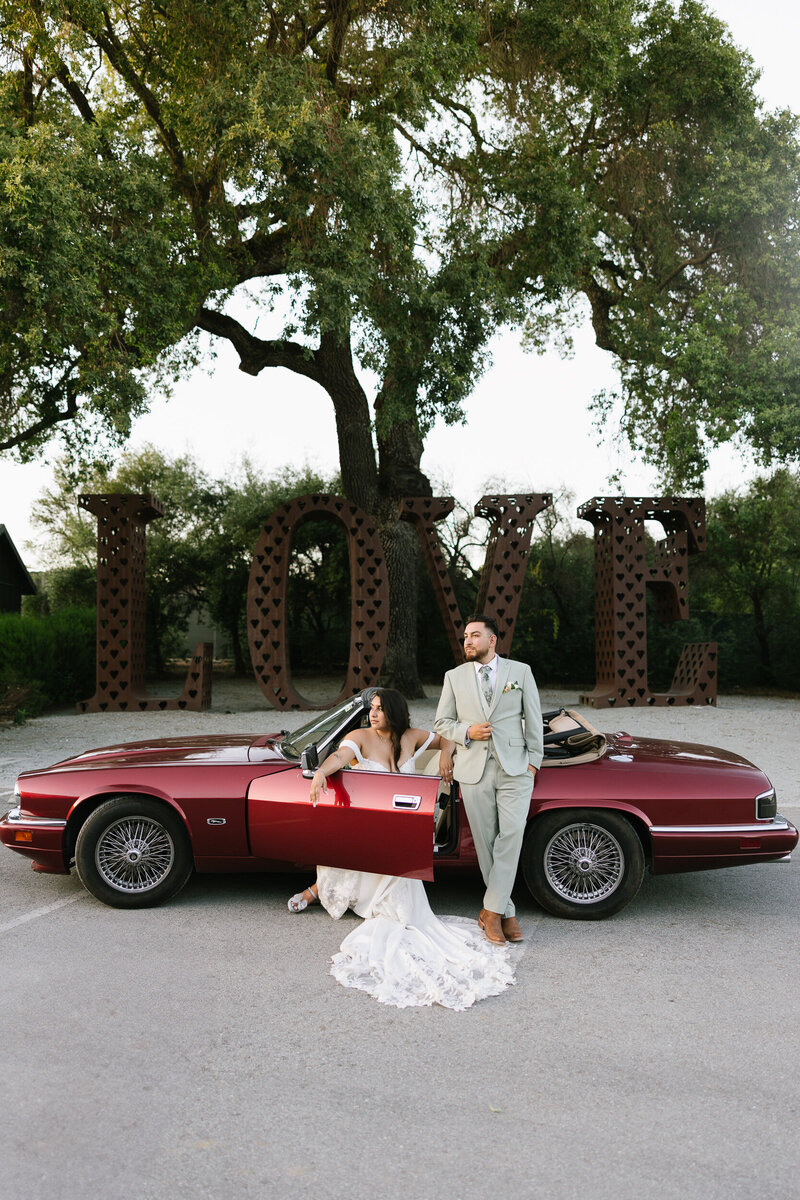 Bride and groom in their classic vintage classic jaguar with a a large metal rusted love sign in the background at MoHi Vineyard