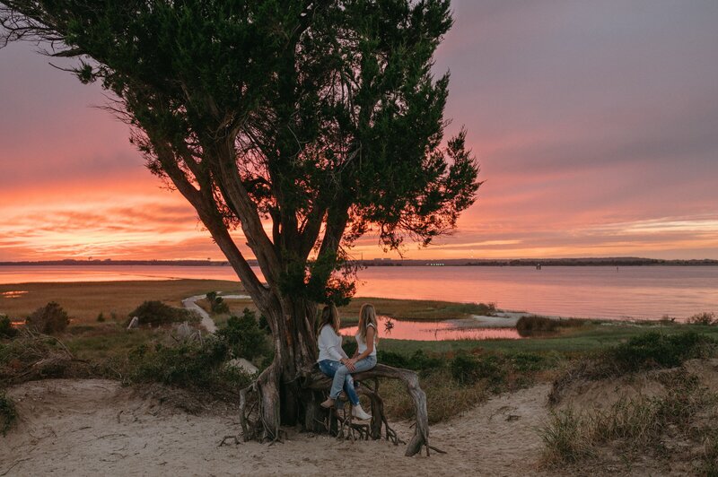 Couple sits under a tree near the beach