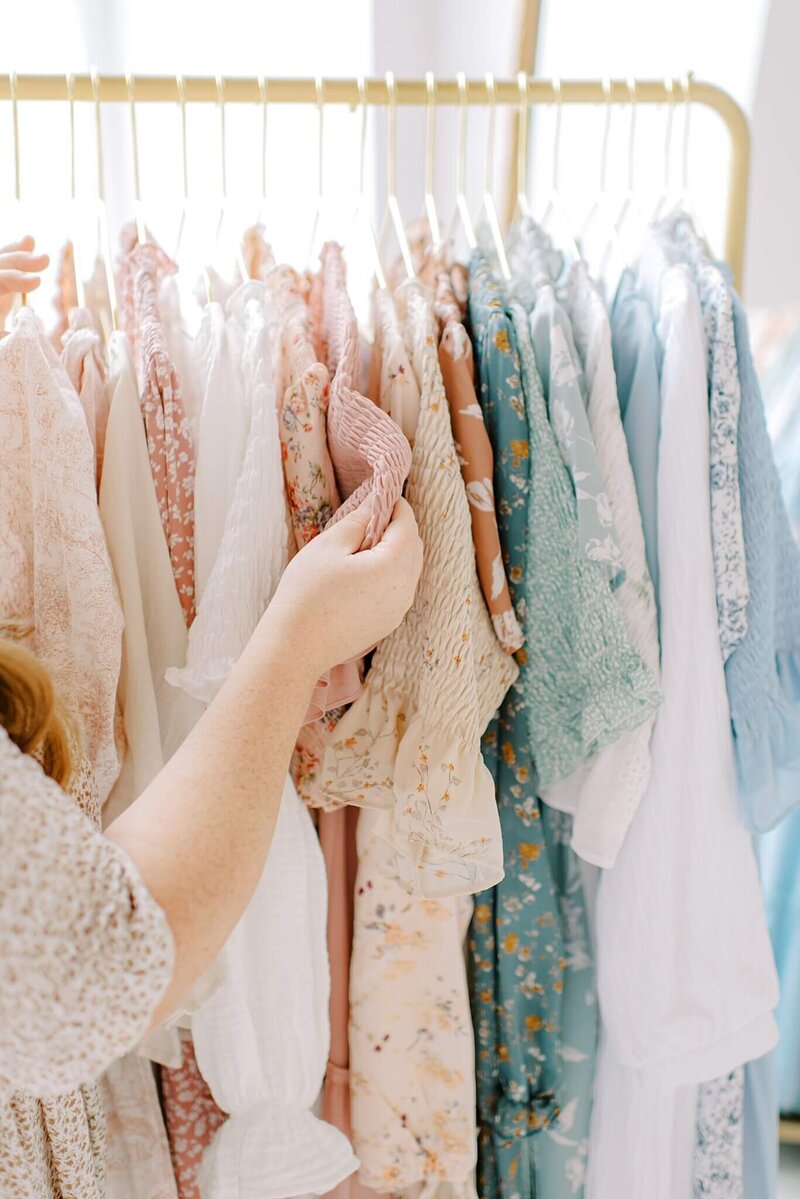 Melissa Mayrie takes a peek at some client dresses hanging on a rack at the studio