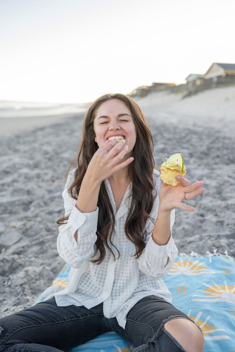 woman sits on beach blanket enjoying a cupcake