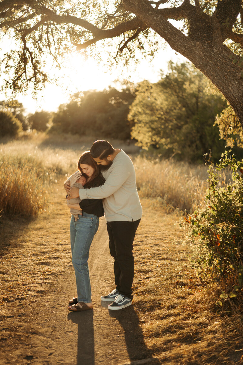 New parents hold their newborn in the golden hour glow.