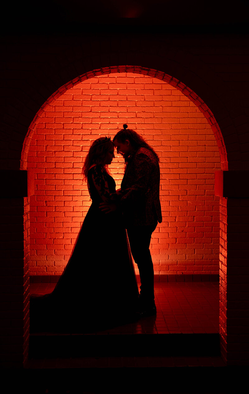 Bride and groom standing on the grand staircase of the Indianapolis War Memorial, holding hands in front of an ornate golden door, with the bride’s dramatic ruffled train cascading down the steps during a luxury downtown wedding.
