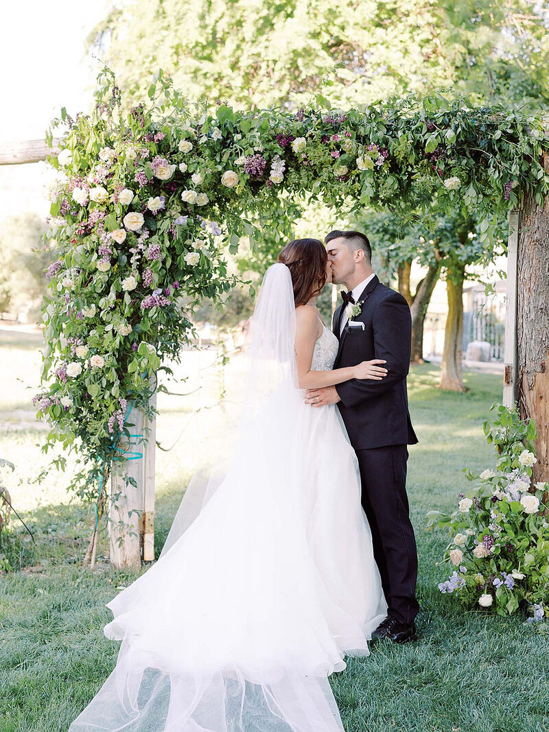 8-radiant-love-events-bride-groom-front-of-floral-alter-kissing-outdoors-romantic-elegant-timeless