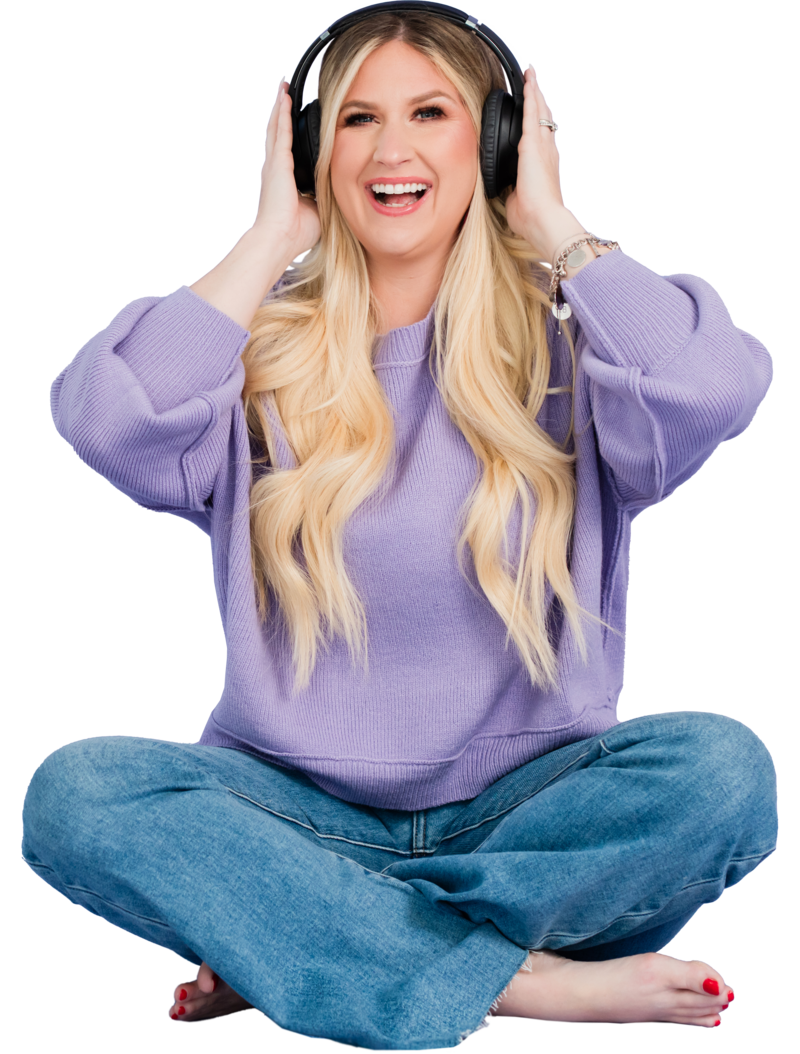 Brittany Kues, owner Kues Media, headshot. Brittany sits crosslegged in jeans and slouchy purple sweater. She wears headphones and is smiling at the camera holding her hands on the headphones over her ears.
