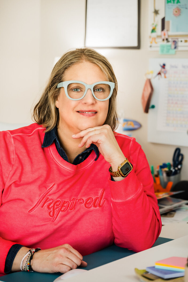 Mya Anderson in glasses and a pink inspired sweater smiles at a desk with colorful office supplies behind her, ready to share The Ultimate College Prep Checklists—your Free Download.
