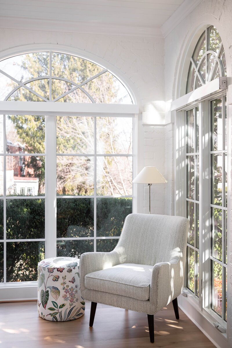 Sunroom with large windows, white armchairs, and a round table, filled with natural light and offering a comfortable seating area.