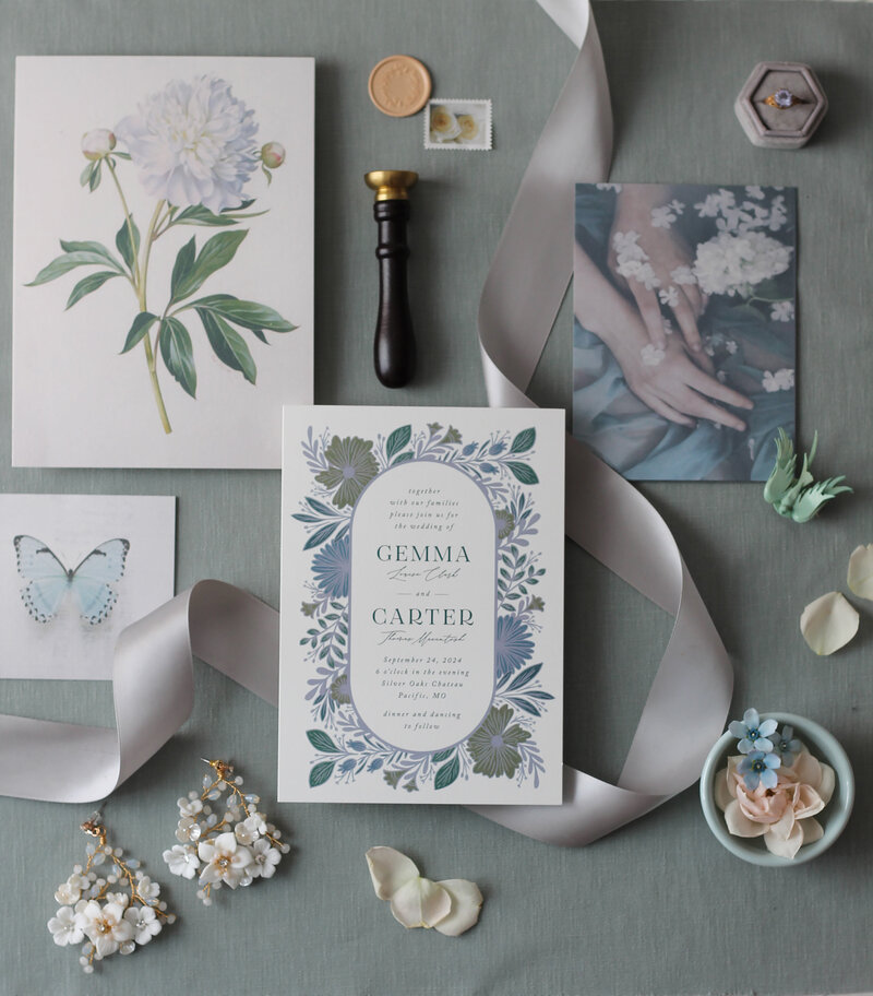 A collection of luxury wedding items including an invitation wax seal and sealing wax stamp, a postage stamp, a botanical drawing of a peony, a velvet ring box with an engagement ring, beaded earrings, a vintage bluebird brooch, satin ribbon, and photographs of butterflies, hands, and textiles