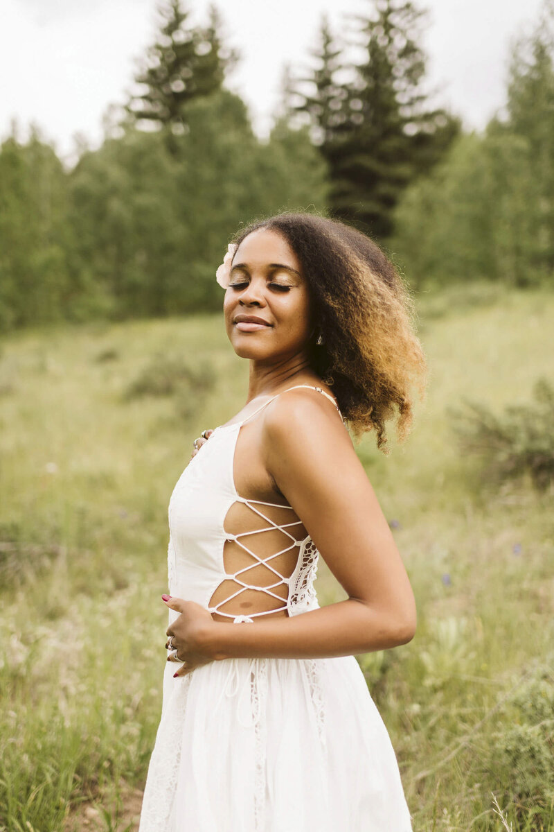 woman wearing a white dress standing in a field with her eyes closed