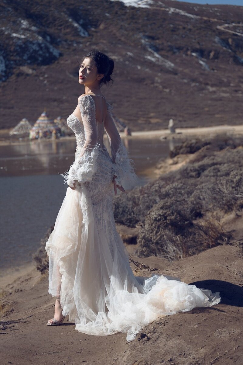 Dramatic shoot of a bride in a haute couture dress by an alpine lake in snow capped mountains.