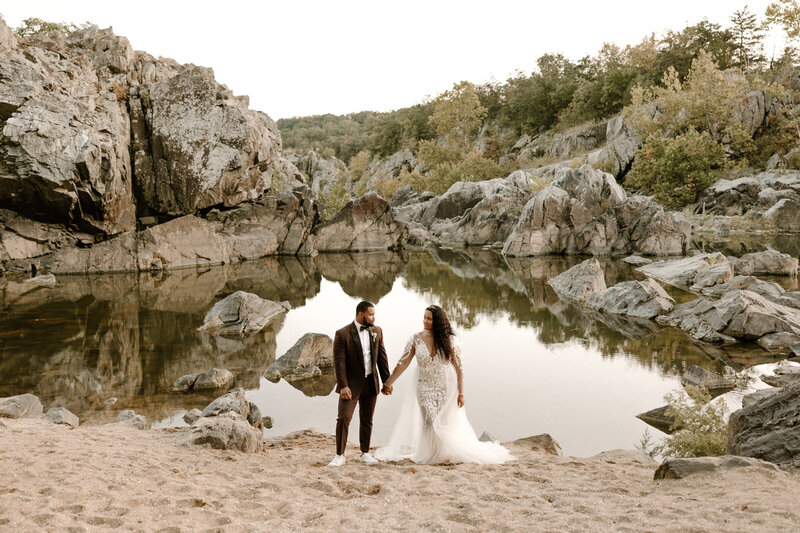 bride and groom holding hands by water