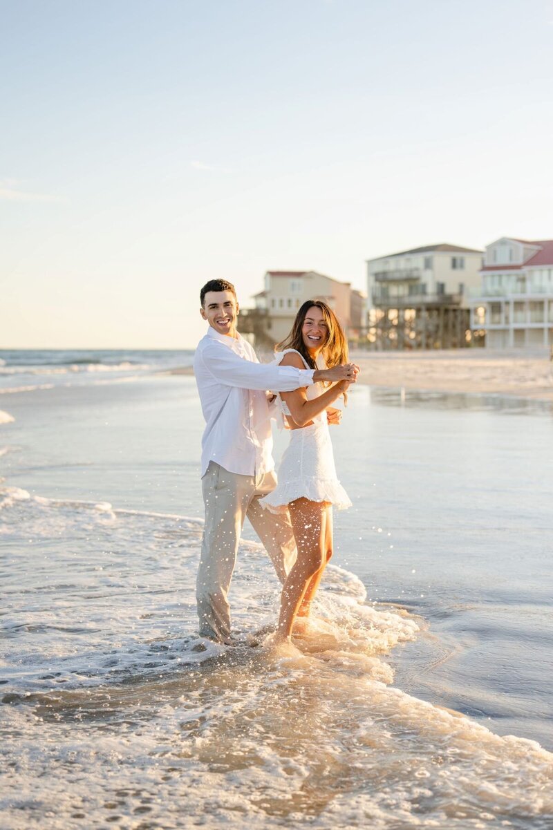 coastal couple dress in white playing in the surf on a beach in north carolina