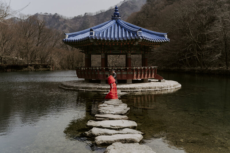 a woman dressed in a red dress crosses the pond at Naejangsa in Korea