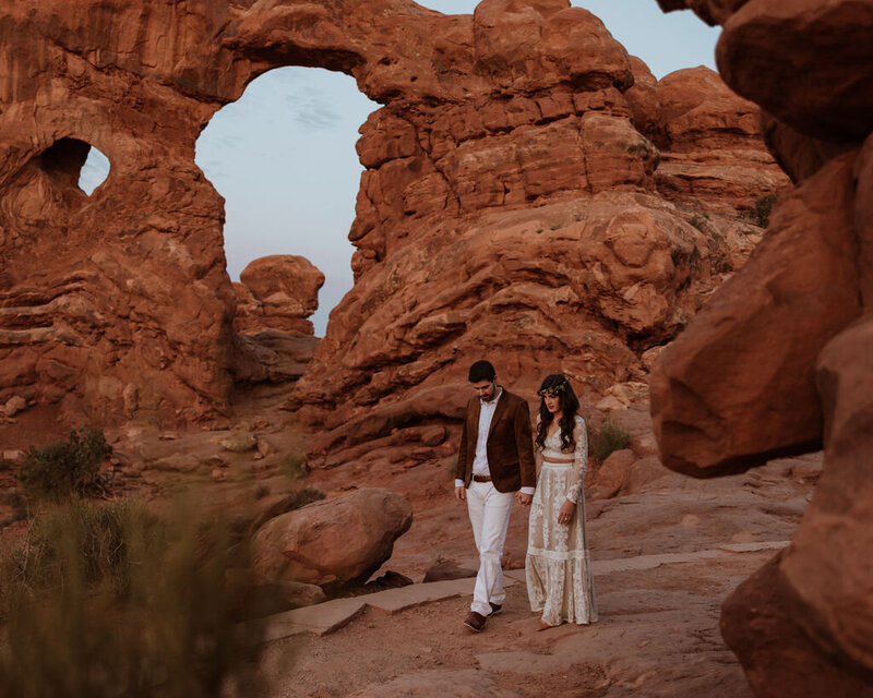 bride and groom walking through large arched rock formations in the desert