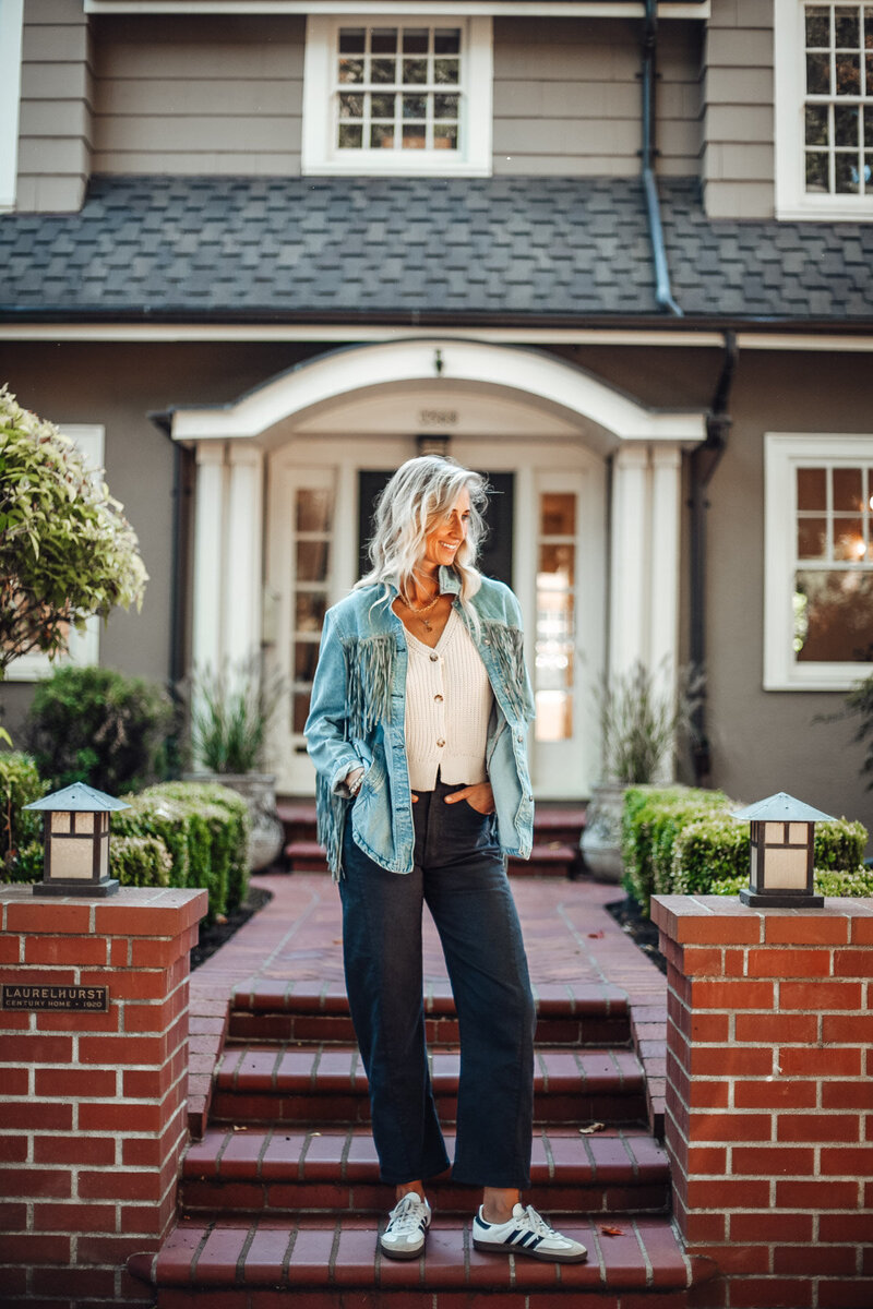 Stephanie, a Portland, OR realtor stands in front of a house with her hands in her pockets.