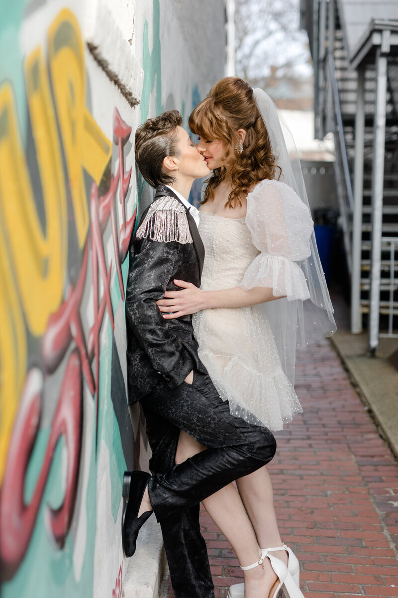 nonbinary wedding couple leaning against a graffiti wall kissing in an alley way in Georgetown DC 