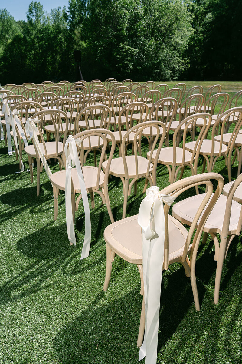 chairs in a ceremony setup on green grass surrounded by trees